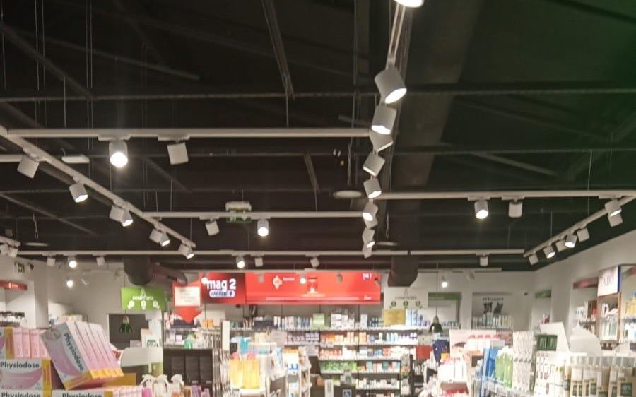 La pharmacie de Nanterre avant relamping : anciens spots halogènes sur rails, plafond sombre